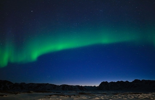 Aerial view of the Aurora Borealis glowing green over snowy mountain peaks and a frozen landscape under a starry night sky in Tasiilaq Sermersooq Municipali Greenland. Aerial view of the Aurora Borealis glowing green over snowy mountain peaks and a frozen landscape under a starry night sky in Tasiilaq Sermersooq Municipali Greenland.