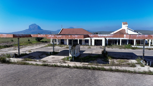 Aerial view of an abandoned roadside building with a weathered canopy and red tiled roof against the backdrop of Platberg mountain in iNtabazwe Free State South Africa. Aerial view of an abandoned roadside building with a weathered canopy and red tiled roof against the backdrop of Platberg mountain in iNtabazwe Free State South Africa.