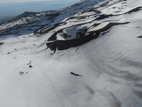 Aerial view of the snow covered volcanic crater on the south slope of Mount Etna with dark volcanic rock and winding mountain roads Nicolosi Sicilia Italy. Aerial view of the snow covered volcanic crater on the south slope of Mount Etna with dark volcanic rock and winding mountain roads Nicolosi Sicilia Italy.