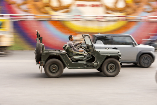 Hanoi Ha Noi Vietnam 11 November 2025 View of a man driving a vintage military style jeep along a city street with a colorful mural in the background.