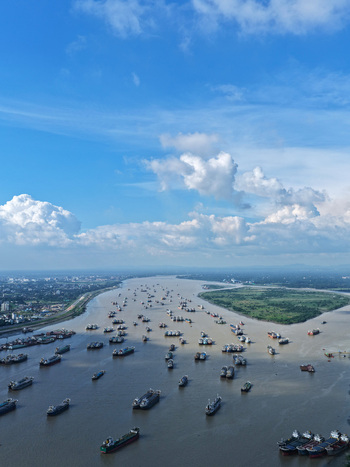 Aerial view of the Karnaphuli River filled with numerous cargo ships and vessels navigating the busy waterway near the lush green banks in Chattogram Chittagong Division Bangladesh.