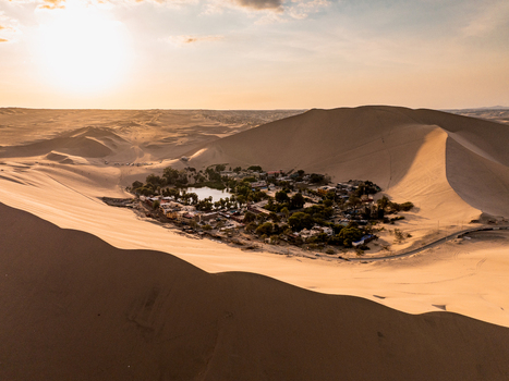 Aerial view of Huacachina oasis surrounded by vast sand dunes under a warm sunset sky Huacachina Ica Peru. Aerial view of Huacachina oasis surrounded by vast sand dunes under a warm sunset sky Huacachina Ica Peru.