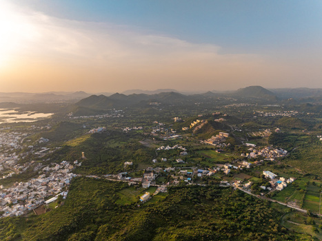 Aerial view of the city of Udaipur nestled among rolling hills and lush greenery during a warm golden hour in Udaipur Rajasthan India.