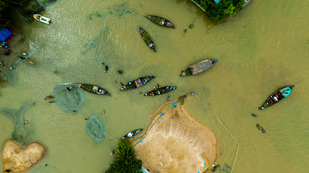 Aerial view of Baish Mowza Sarak Bazar with wooden boats navigating through the river sandbanks and people working in the water in Nabinagar Chittagong Division Bangladesh. Aerial view of Baish Mowza Sarak Bazar with wooden boats navigating through the river sandbanks and people working in the water in Nabinagar Chittagong Division Bangladesh.