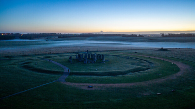 Aerial view of Stonehenge surrounded by rolling fields and morning mist under a clear twilight sky in Salisbury England United Kingdom. Aerial view of Stonehenge surrounded by rolling fields and morning mist under a clear twilight sky in Salisbury England United Kingdom.