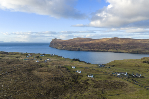 Aerial view of the coastal village of Milovaig with white cottages scattered across the rugged landscape overlooking the blue waters of the sea Milovaig Scotland United Kingdom.