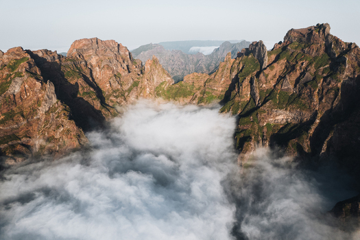 Aerial view of jagged peaks emerge triumphantly from a sea of ethereal clouds the sunlight painting the rugged landscape with hues of gold and umber Pico do Areeiro Madeira Portugal.