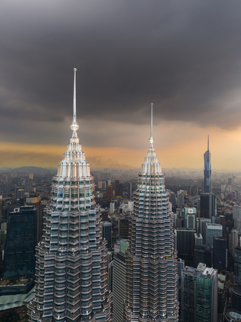 Kuala Lumpur Malaysia 11 March 2026 Aerial view of the Petronas Twin Towers rising above the city skyline under a dramatic stormy sky at sunset.