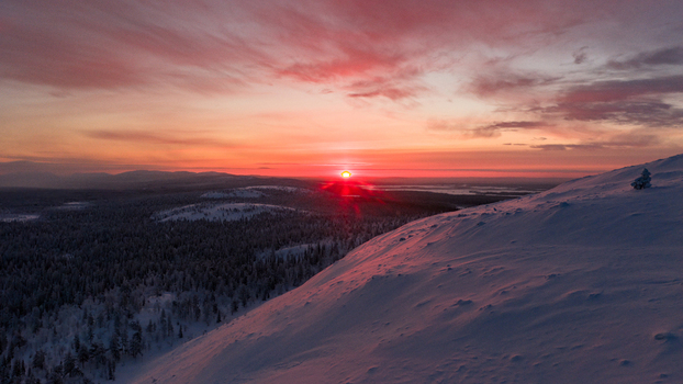 Aerial view of Luosto fell with snow covered slopes and vast taiga forest under a vibrant red sunset sky Sodankyla Lapland Finland. Aerial view of Luosto fell with snow covered slopes and vast taiga forest under a vibrant red sunset sky Sodankyla Lapland Finland.