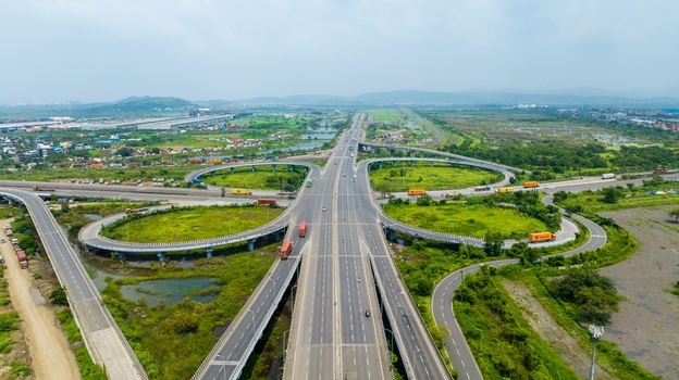 Aerial view of the JNPT Interchange featuring multi level highway ramps surrounding green landscapes and industrial areas with trucks on the road in Navi Mumbai Maharashtra India.