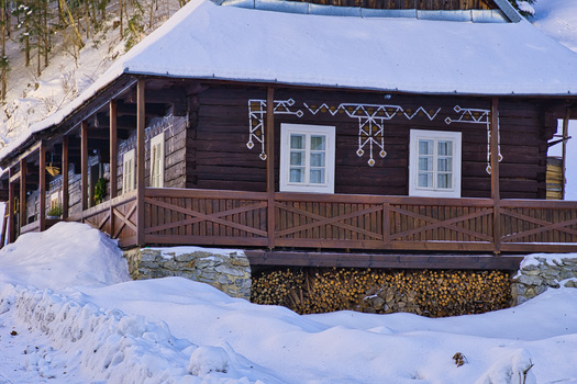 View of a rustic wooden house adorned with delicate white trim and a blanket of snow stands serene against the backdrop of a winter forest Moce Slovakia.