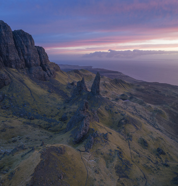 Aerial view of the dramatic rock pinnacles of The Storr overlooking the grassy slopes and the sea under a colorful sunset sky in Isle of Skye Scotland United Kingdom. Aerial view of the dramatic rock pinnacles of The Storr overlooking the grassy slopes and the sea under a colorful sunset sky in Isle of Skye Scotland United Kingdom.