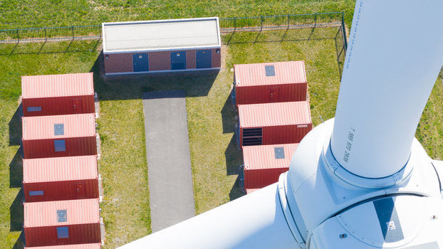 Aerial view of Energiepark Haringvliet Zuid featuring a wind turbine base red storage containers and a brick utility building on green grass in Middelharnis South Holland Netherlands.