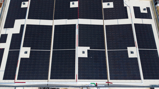 Aerial view of a modern logistics warehouse roof featuring extensive solar panel arrays ventilation systems and white roofing membranes in Melegnano Lombardy Italy.