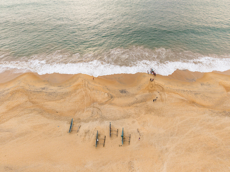 Aerial view of traditional outrigger boats on a golden sandy beach with turquoise ocean waves and people in Galle Southern Province Sri Lanka.