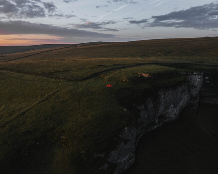 Aerial view of a red tent pitched on the grassy edge of the limestone cliffs at Winnats Pass during the golden hour in Hope Valley England United Kingdom. Aerial view of a red tent pitched on the grassy edge of the limestone cliffs at Winnats Pass during the golden hour in Hope Valley England United Kingdom.