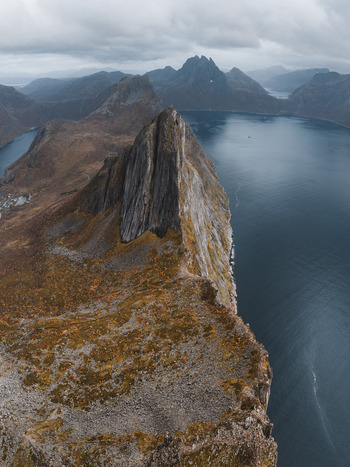 Aerial view of the dramatic Segla mountain peak rising above the dark waters of the fjord with rugged cliffs and autumn colored terrain in Senja Troms Norway.