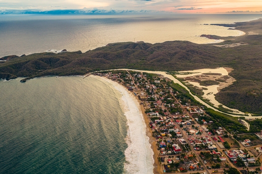 Aerial view of Playa Punta Perula featuring the sandy coastline coastal town buildings and lush hills meeting the ocean in Perula Jalisco Mexico. Aerial view of Playa Punta Perula featuring the sandy coastline coastal town buildings and lush hills meeting the ocean in Perula Jalisco Mexico.