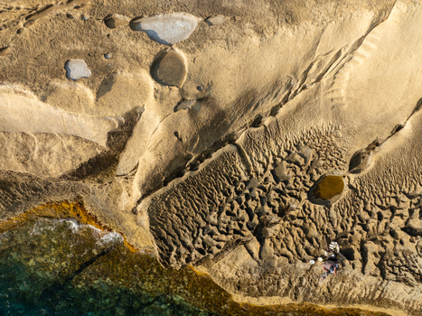 Aerial view of the rugged coastline where golden rocks meet the turquoise sea creating a mesmerizing contrast of textures and tones Mykonos Greece. Aerial view of the rugged coastline where golden rocks meet the turquoise sea creating a mesmerizing contrast of textures and tones Mykonos Greece.