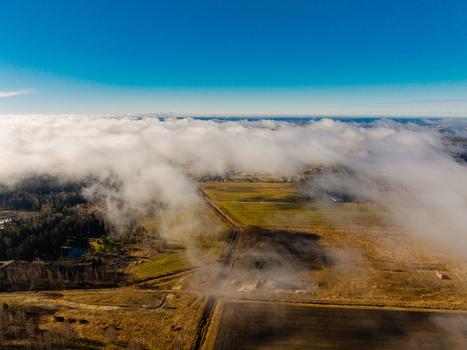 Aerial view of fields forest and the A8 highway partially covered by low hanging clouds under a clear blue sky in Olaine parish Olaine Municipality Latvia. Aerial view of fields forest and the A8 highway partially covered by low hanging clouds under a clear blue sky in Olaine parish Olaine Municipality Latvia.