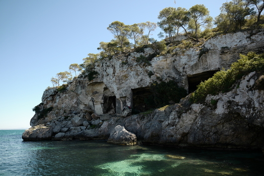 View of the rocky cliffs and sea caves of Mallorca with pine trees on the ridge and clear turquoise water in Balearic Islands Spain.