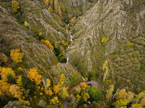 Aerial view of the Poco do Inferno waterfall cascading through a rocky canyon with vibrant autumn foliage and steep cliffs in Manteigas Guarda District Portugal. Aerial view of the Poco do Inferno waterfall cascading through a rocky canyon with vibrant autumn foliage and steep cliffs in Manteigas Guarda District Portugal.