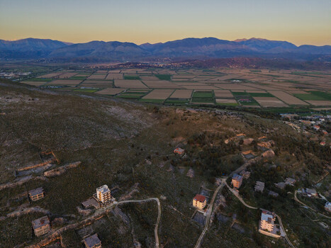 Aerial view of the agricultural fields and rolling hills near Saranda with scattered buildings illuminated by the warm light of sunset in Saranda Vlore County Albania. Aerial view of the agricultural fields and rolling hills near Saranda with scattered buildings illuminated by the warm light of sunset in Saranda Vlore County Albania.