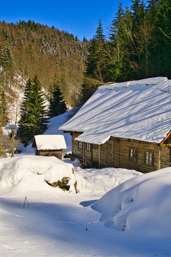 View of a rustic cabin nestled under a blanket of snow contrasted by the vibrant evergreens and the clear blue sky Moce Banska Bystrica Region Slovakia.