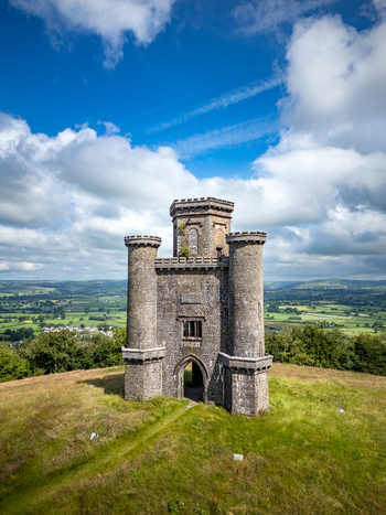Aerial view of Paxton s Tower standing on a grassy hilltop overlooking the lush green Towy Valley under a blue sky with white clouds in Llanarthney Wales United Kingdom.