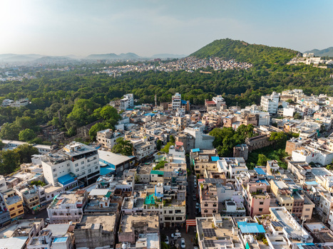 Aerial view of the dense urban landscape of Udaipur featuring traditional rooftops narrow streets and lush green hills in the background in Udaipur Rajasthan India.