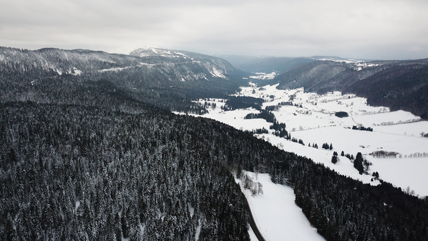 Aerial view of La Vattay in the snow covered Jura Mountains with dense pine forests and open winter fields in Mijoux Auvergne Rhone Alpes France. Aerial view of La Vattay in the snow covered Jura Mountains with dense pine forests and open winter fields in Mijoux Auvergne Rhone Alpes France.