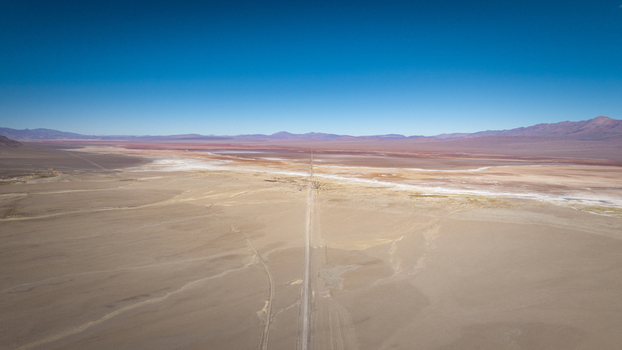 Aerial view of a long straight road cutting through the vast arid desert landscape with distant mountains under a clear blue sky in Argentina. Aerial view of a long straight road cutting through the vast arid desert landscape with distant mountains under a clear blue sky in Argentina.
