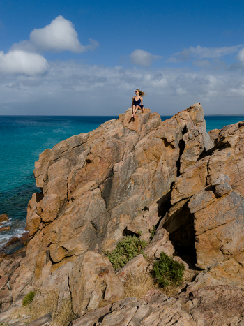 Aerial view of a woman sitting on Castle Rock overlooking the turquoise ocean in Dunsborough Western Australia Australia. Aerial view of a woman sitting on Castle Rock overlooking the turquoise ocean in Dunsborough Western Australia Australia.