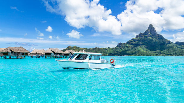 View of a white motorboat cruising on the turquoise lagoon with overwater bungalows and Mount Otemanu in the background in Bora Bora Leeward Islands French Polynesia.