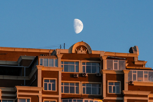 View of a residential building with a crown shaped architectural detail on the roof under a clear blue sky with a visible half moon in Aktau Mangystau Region Kazakhstan.
