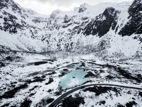 Aerial view of the snow covered peaks of Grotfjord featuring a turquoise glacial lake and a winding road through the arctic landscape in Tromvik Troms Norway. Aerial view of the snow covered peaks of Grotfjord featuring a turquoise glacial lake and a winding road through the arctic landscape in Tromvik Troms Norway.