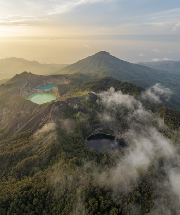 Aerial view of the volcanic crater lakes of Kelimutu National Park with vibrant turquoise and dark waters surrounded by lush mountains and clouds in Detusoko East Nusa Tenggara Indonesia.