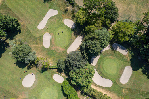Aerial view of a golf course with green fairways sand bunkers and golfers surrounded by lush trees in Turin Piedmont Italy. Aerial view of a golf course with green fairways sand bunkers and golfers surrounded by lush trees in Turin Piedmont Italy.