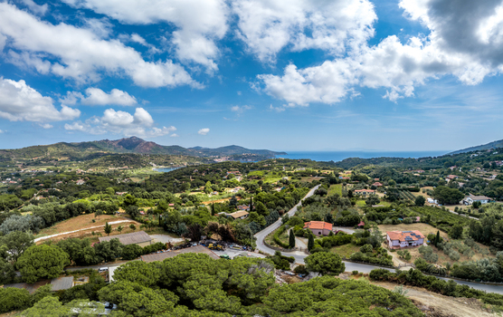 Aerial view of the lush landscape and rolling hills surrounding Porto Azzurro with scattered houses winding roads and the sea in the distance in Porto Azzurro Toscana Italy.