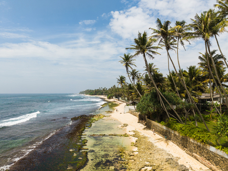 Aerial view of Thalpe Beach with people walking along the shore near tall palm trees and turquoise ocean waves crashing against the reef Talpe Southern Province Sri Lanka. Aerial view of Thalpe Beach with people walking along the shore near tall palm trees and turquoise ocean waves crashing against the reef Talpe Southern Province Sri Lanka.