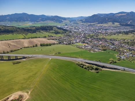 Aerial view of the D1 motorway viaduct crossing vibrant green fields with the town and rolling mountains under a clear blue sky Likavka Zilina Region Slovakia. Aerial view of the D1 motorway viaduct crossing vibrant green fields with the town and rolling mountains under a clear blue sky Likavka Zilina Region Slovakia.