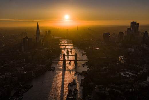 Aerial view of Tower Bridge spanning the River Thames with The Shard and city skyline silhouetted against a golden sunset in London Greater London United Kingdom. Aerial view of Tower Bridge spanning the River Thames with The Shard and city skyline silhouetted against a golden sunset in London Greater London United Kingdom.