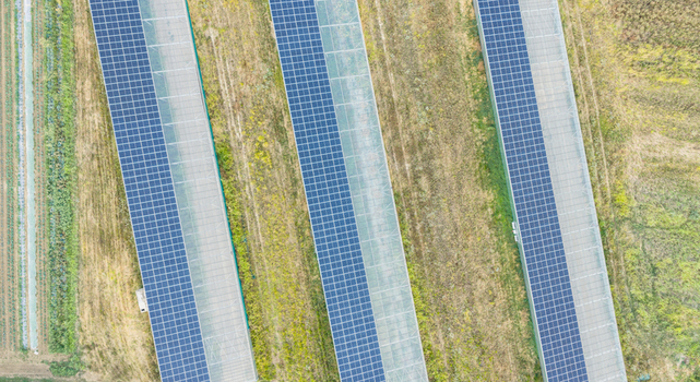 Aerial view of agricultural greenhouses with rooftop photovoltaic solar panels in rural fields illustrating agrivoltaics and renewable energy in Loriol sur Drome Auvergne Rhone Alpes France.