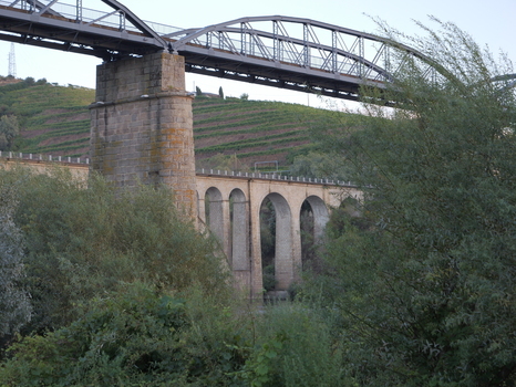 View of the historic stone arch viaduct and metal railway bridge spanning the landscape with terraced vineyards in the background in Peso da Regua Vila Real District Portugal.