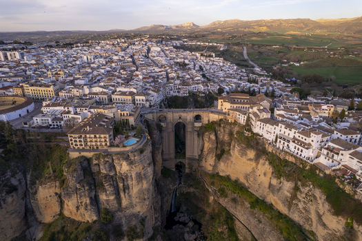 Aerial view of the historic Puente Nuevo bridge spanning the deep El Tajo gorge with white buildings and sunset light in Ronda Andalusia Spain. Aerial view of the historic Puente Nuevo bridge spanning the deep El Tajo gorge with white buildings and sunset light in Ronda Andalusia Spain.