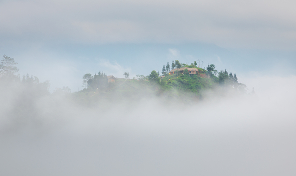 Aerial view of small houses perched on a lush green hilltop emerging from a thick blanket of morning fog in the mountains Hoang Su Phi Ha Giang Vietnam. Aerial view of small houses perched on a lush green hilltop emerging from a thick blanket of morning fog in the mountains Hoang Su Phi Ha Giang Vietnam.
