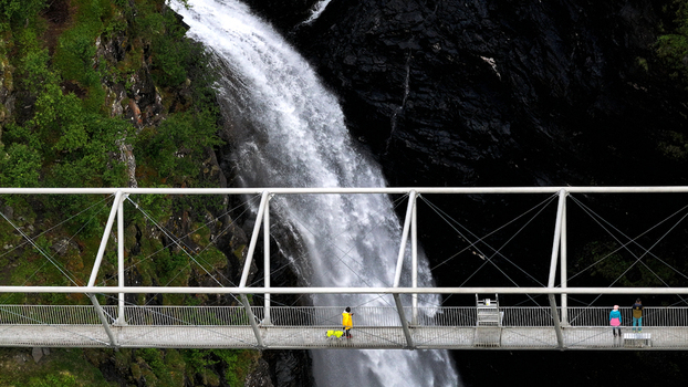 Aerial view of Gorsa bridge spanning a deep canyon with a waterfall cascading below surrounded by lush vegetation and rocky cliffs with people walking in Birtavarre Troms Norway. Aerial view of Gorsa bridge spanning a deep canyon with a waterfall cascading below surrounded by lush vegetation and rocky cliffs with people walking in Birtavarre Troms Norway.
