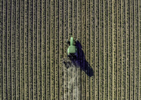 Aerial view of a green tractor cultivating a large agricultural field with straight crop rows in Palm Desert California United States. Aerial view of a green tractor cultivating a large agricultural field with straight crop rows in Palm Desert California United States.