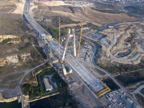 Aerial view of a large cable stayed bridge under construction with tall yellow cranes concrete pillars and surrounding hilly terrain in Istanbul Istanbul Turkiye.