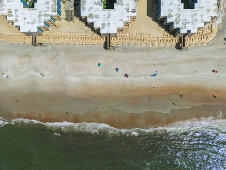 Aerial view of beachfront buildings with sandbag fortifications along the shoreline with people on the sand and Atlantic Ocean waves in North Topsail Beach North Carolina United States.